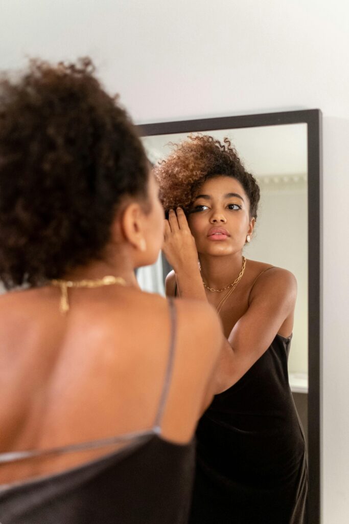 The Fear of Being Seen: A Strategic Guide for New Beginnings 3 A woman in a new outfit looks into a mirror, and her reflection smiles confidently back, symbolising the psychological process of habituation and style acceptance.
