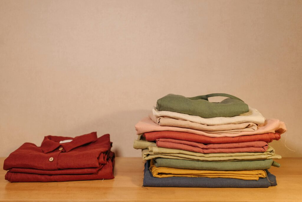 Neatly folded piles of clothes on a bed during a closet audit, a crucial step to build personal style.