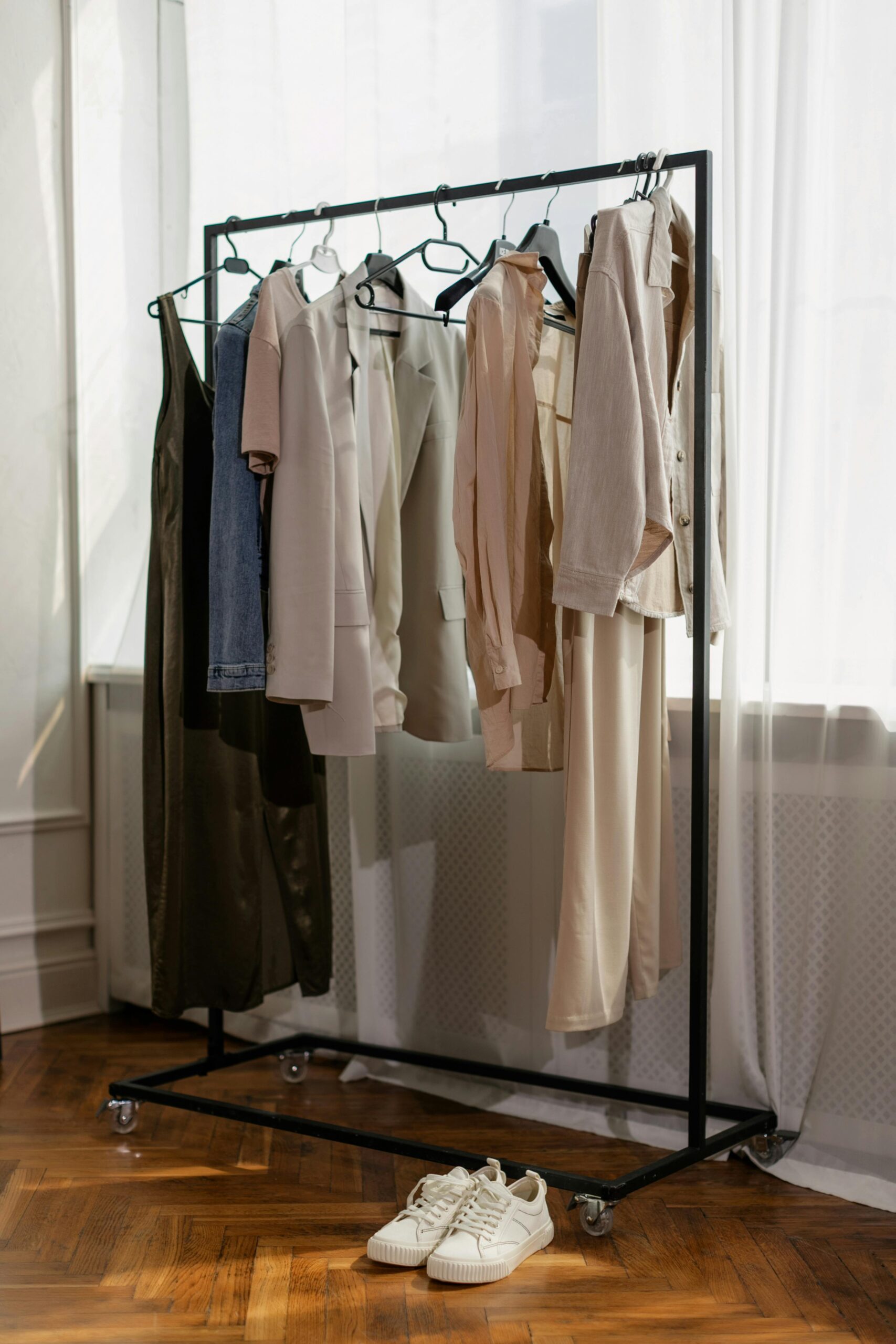 A single tailored wool coat hanging in a sunlit room, representing the simplicity of a curated winter capsule.